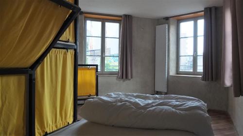 a bedroom with a bed in a room with windows at La Maison Rouge - Backpacker Hostel in Saint-Étienne