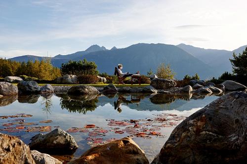 a person sitting on a rock next to a pond at Hotel Lärchenhof Natur in Seefeld in Tirol
