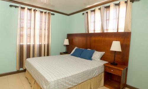 a bedroom with a bed with a wooden headboard and windows at Believe Caribbean Apartment in Bridgetown