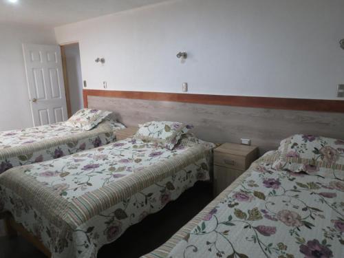 two beds in a hotel room with floral sheets at Residencial Victoria Said in Linares