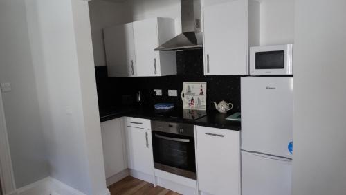 a kitchen with white cabinets and a white refrigerator at Portum -John St Apartment in Helensburgh