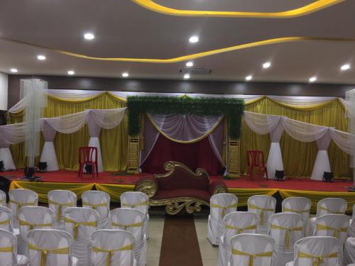 a stage with white chairs and a bed in a room at Hotel Pooja International in Dāvangere