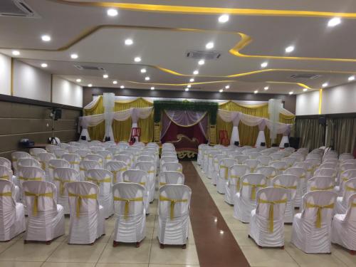 a banquet hall with white chairs and a stage at Hotel Pooja International in Dāvangere
