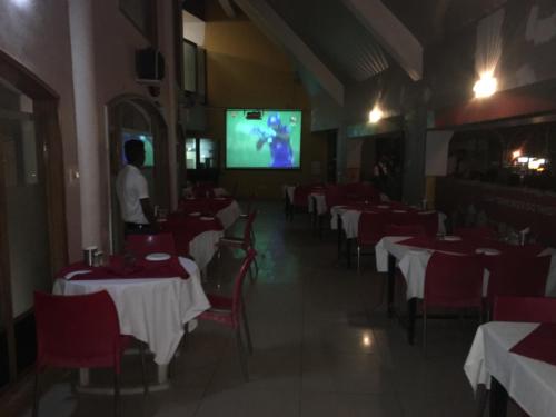 a man standing in a restaurant with tables and a tv at Hotel Pooja International in Dāvangere