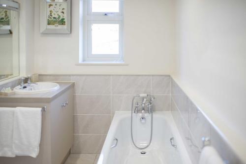 Baño blanco con bañera y lavamanos en Cowdray Holiday Cottages, en Midhurst