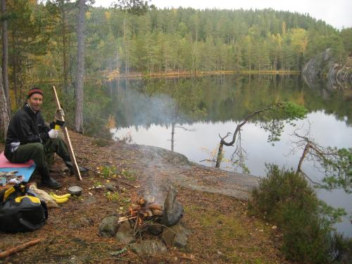 a man sitting next to a fire next to a lake at Tivedens Hostel-Vandrarhem in Karlsborg