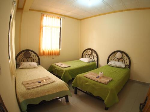 a room with two beds with green sheets and a window at Hostal Butch Cassidy in Tupiza