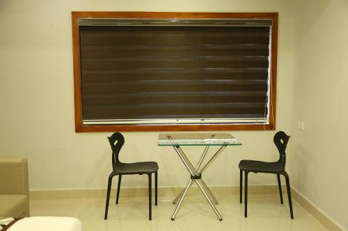 2 sillas y una mesa de cristal en una habitación con ventana en 4U Business Hotel en Chennai