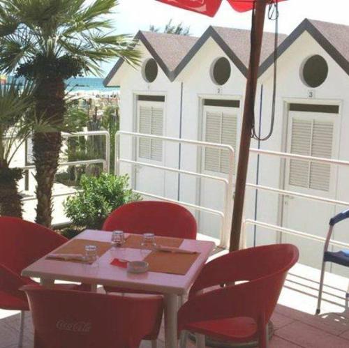 a table with red chairs and an umbrella on a balcony at Hotel Blumen in San Benedetto del Tronto