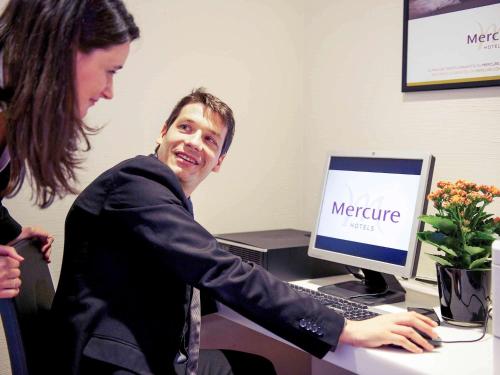 a woman assisting a man in front of a computer at Hotel Mercure Milano Solari in Milan