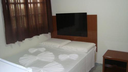 a bedroom with a bed with white sheets and a flat screen tv at Hotel Porto Real in Pôrto Real