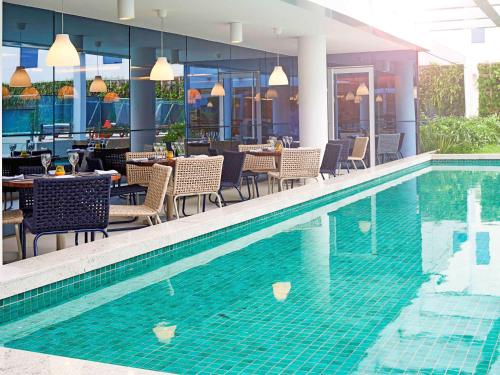 a swimming pool with tables and chairs next to a restaurant at Novotel Rio de Janeiro Parque Olimpico in Rio de Janeiro