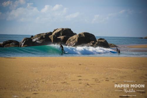 a man riding a wave on a surfboard on the beach at Paper Moon Kudils in Arugam Bay