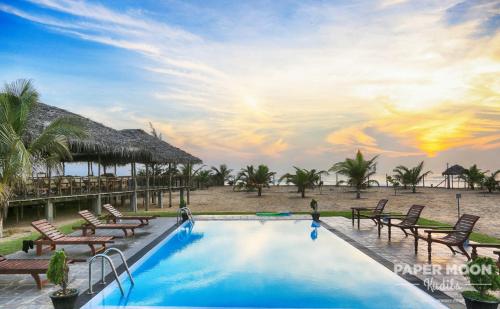 a resort swimming pool with chairs and a sunset at Paper Moon Kudils in Arugam Bay
