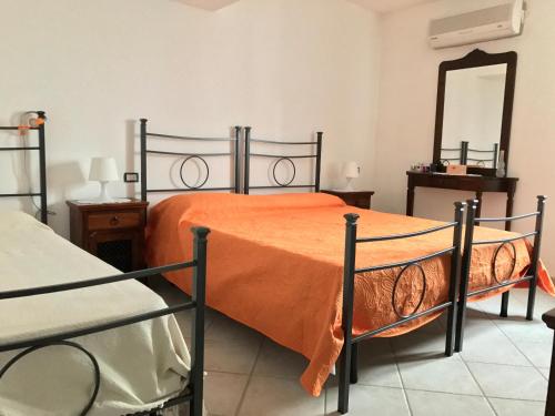 a bedroom with a bed with an orange comforter and a mirror at Affittacamere Peonia in Oliena