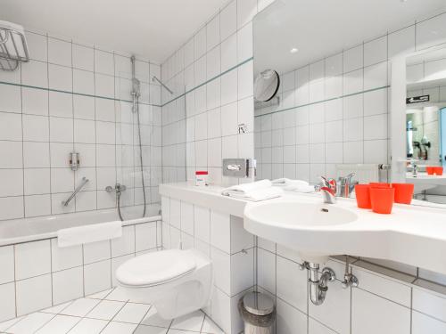 a white bathroom with a toilet and a sink at DORMERO Hotel Dresden Airport in Dresden