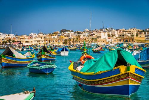 a group of boats in the water with buildings in the background at St. Peter's Pool Holiday Apartment in Marsaxlokk