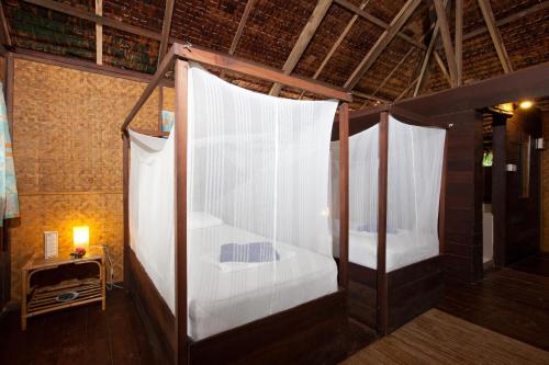 two beds in a room with white curtains at Rimba Resort - Dive Centre & Spa in Pulau Sibu
