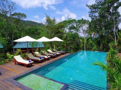 a swimming pool with lounge chairs and umbrellas at Niraamaya Retreats Cardamom Club in Thekkady