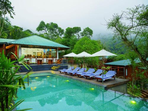 a swimming pool with lounge chairs and umbrellas at Niraamaya Retreats Cardamom Club in Thekkady