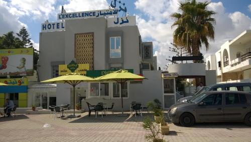 une voiture garée devant un hôtel avec des tables et des parasols dans l'établissement Hotel Excellence, à Tunis