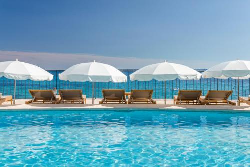 a swimming pool with chairs and umbrellas at Hôtel Le Bailli De Suffren in Rayol-Canadel-sur-Mer