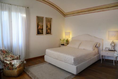 a white bedroom with a bed and a chair at Villa Foscarini Cornaro in Gorgo al Monticano