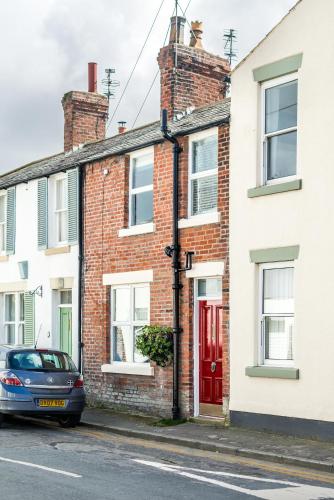 a car parked in front of a brick house with a red door at Lobster Cottage Lytham in Lytham St Annes
