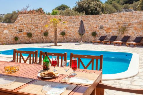 a wooden table with wine glasses next to a swimming pool at Villa Roza Murter in Murter