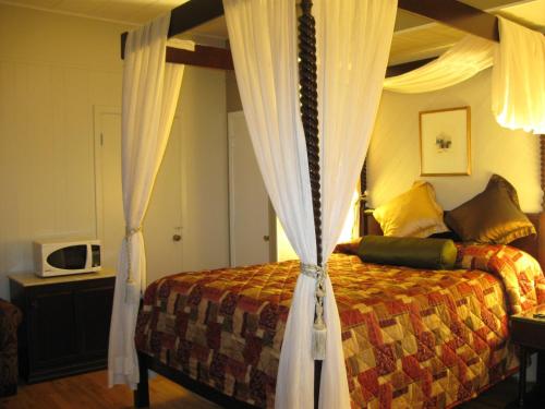 Motel Clair Mont في سانت-أغاث-دي-مونت: غرفة نوم مع سرير مظلة مع ستائر وميكروويف