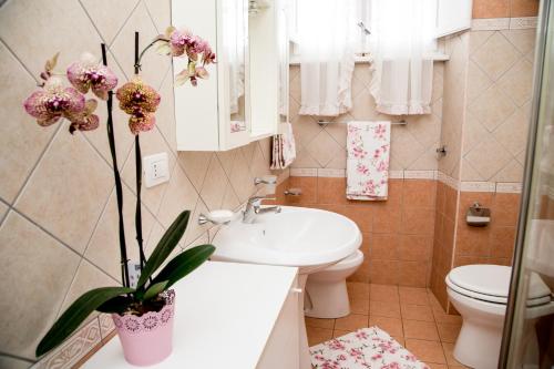 baño con lavabo, aseo y jarrón con flores en Casa Fertilia, en Fertilia
