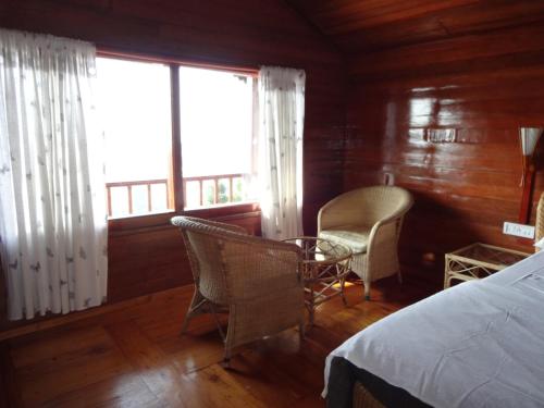 a bedroom with a bed and two chairs and a window at Surya Holidays Kodaikanal in Kodaikānāl
