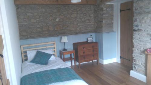 a bedroom with a bed and a dresser and a stone wall at Brynawel in Saint Dogmaels