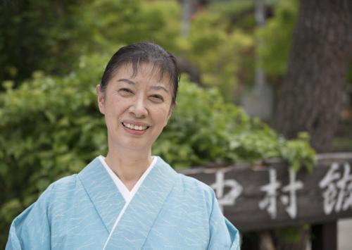 a woman in a kimono standing in front of a sign at Nakamurakan in Takayama