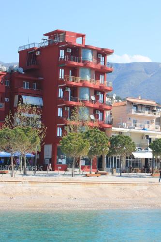 um edifício vermelho com árvores em frente a uma praia em Hotel Veizi em Himare