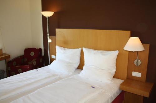 a bed with white sheets and pillows next to a lamp at Pension Geno in Geisenhausen
