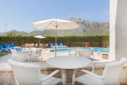 a table and chairs with an umbrella next to a pool at Apartamentos Massol in Port de Pollensa
