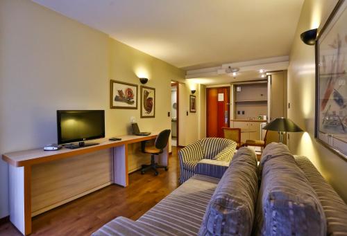 a living room with a couch and a desk with a television at Metropolitan Hotel Brasília in Brasilia