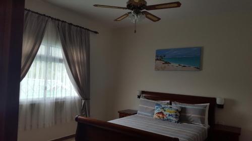 a bedroom with a bed with a ceiling fan and a window at Seashell Beach Villa in Grand'Anse Praslin