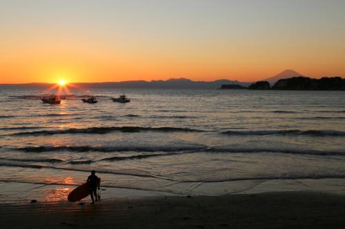 a man standing on the beach with a surfboard at sunset at Guest House Kamejikan -turtle time- in Kamakura