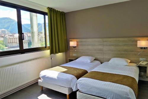 two beds in a hotel room with a window at Jura Hotel Restaurant Le Panoramic in Saint-Claude