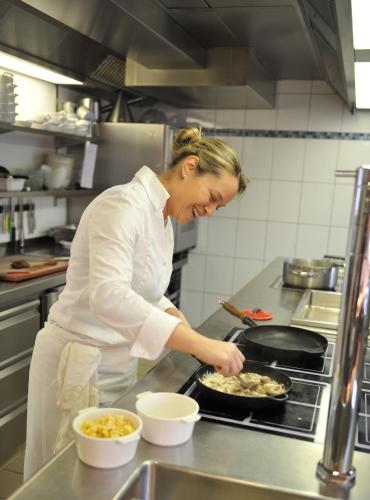 a woman in a kitchen preparing food in a pan at Restaurant A l'Aigle in Wimmenau