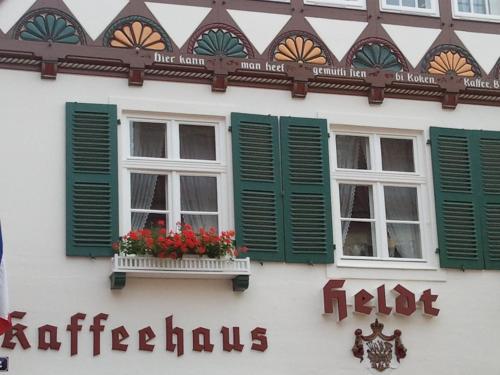 a white building with green shuttered windows and red flowers at Apartments im Kaffeehaus Heldt in Eckernförde