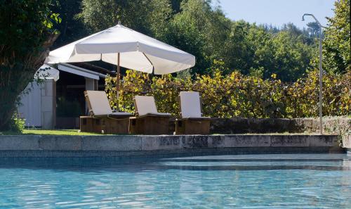 duas cadeiras e um guarda-sol junto a uma piscina em Fervenza Casa Grande & Restaurante em Reguengo