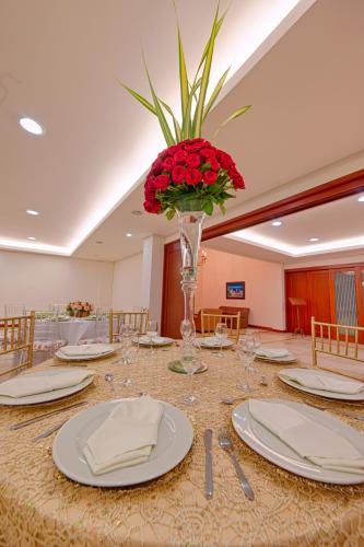 a table with plates and a vase with red flowers at Hotel Obelisco in Cali