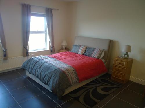 a bedroom with a bed with a red blanket and a window at 1 Bayview in Glenariff
