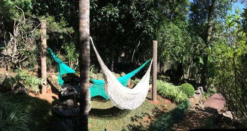 a hammock hanging from two trees in a garden at Hospedagem Casadalee chalé com piscina privativa aquecida e Apartamento sem piscina in Monte Verde