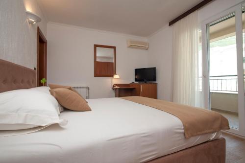 a bedroom with a large white bed and a television at Guest House Medin in Petrovac na Moru