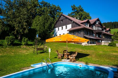 a pool with an umbrella and chairs and a house at Chata Pod lipami in Rokytnice nad Jizerou