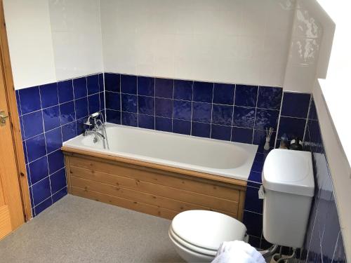 a bathroom with a tub and a toilet and blue tiles at Dunnottar Woods Cottage in Stonehaven